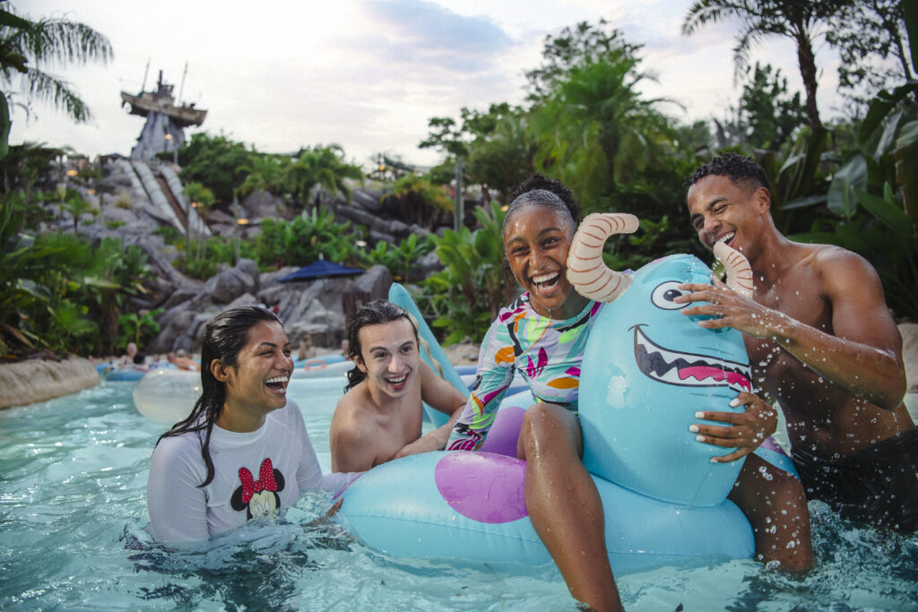 Family enjoying the water at Typhoon Lagoon. A child is sitting on a Sulley from Monsters Inc float. The famous wrecked ship on the tip of the mountain is in the background.