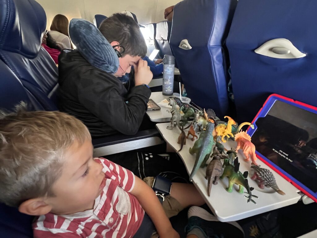 Small child watching a tablet and playing with dinosaurs on a plane.