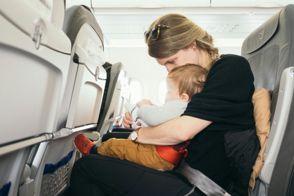 A mom holding a baby on an airplane while sitting.