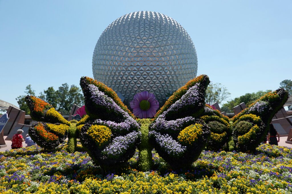 Epcot's large sphere building behind butterfly shaped plants and flowers