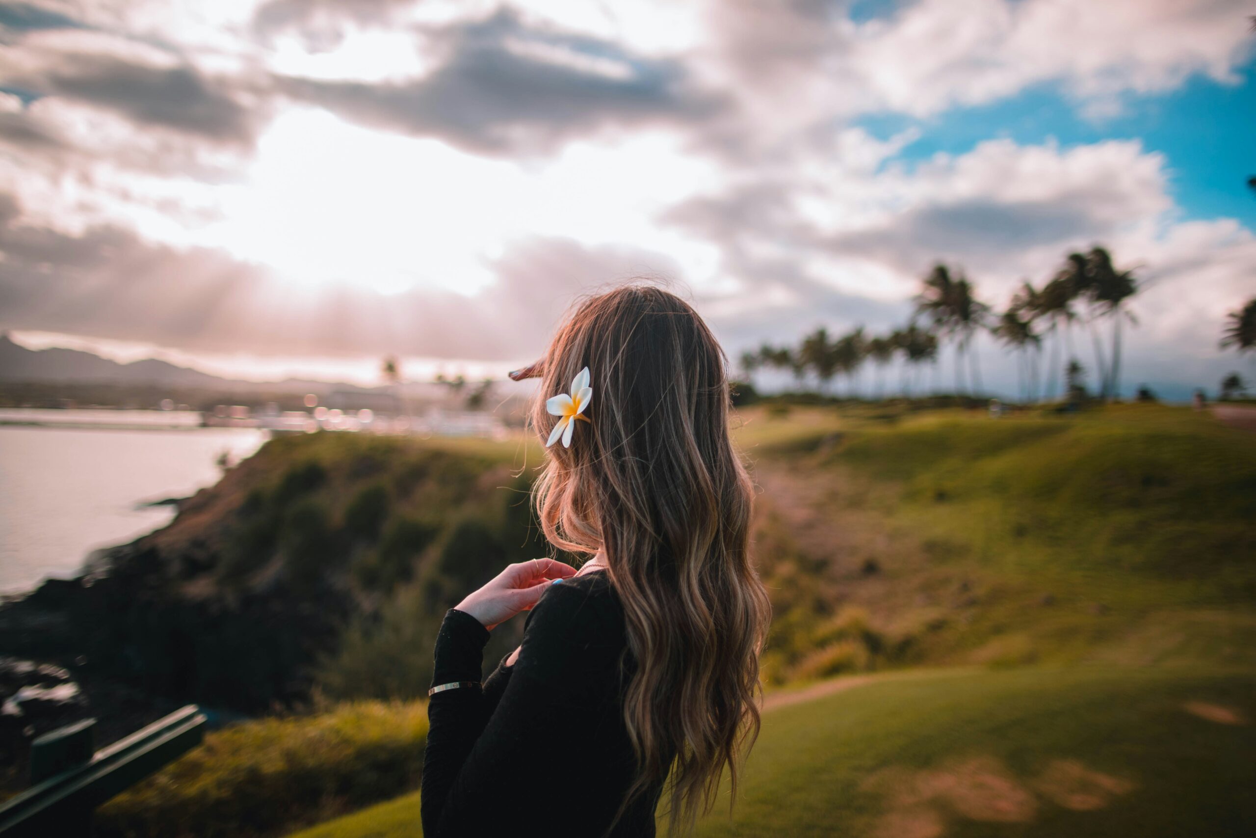 Women with a white flower in her long brown hair has her head turned away from the camera and is looking at the Hawaiian coast.